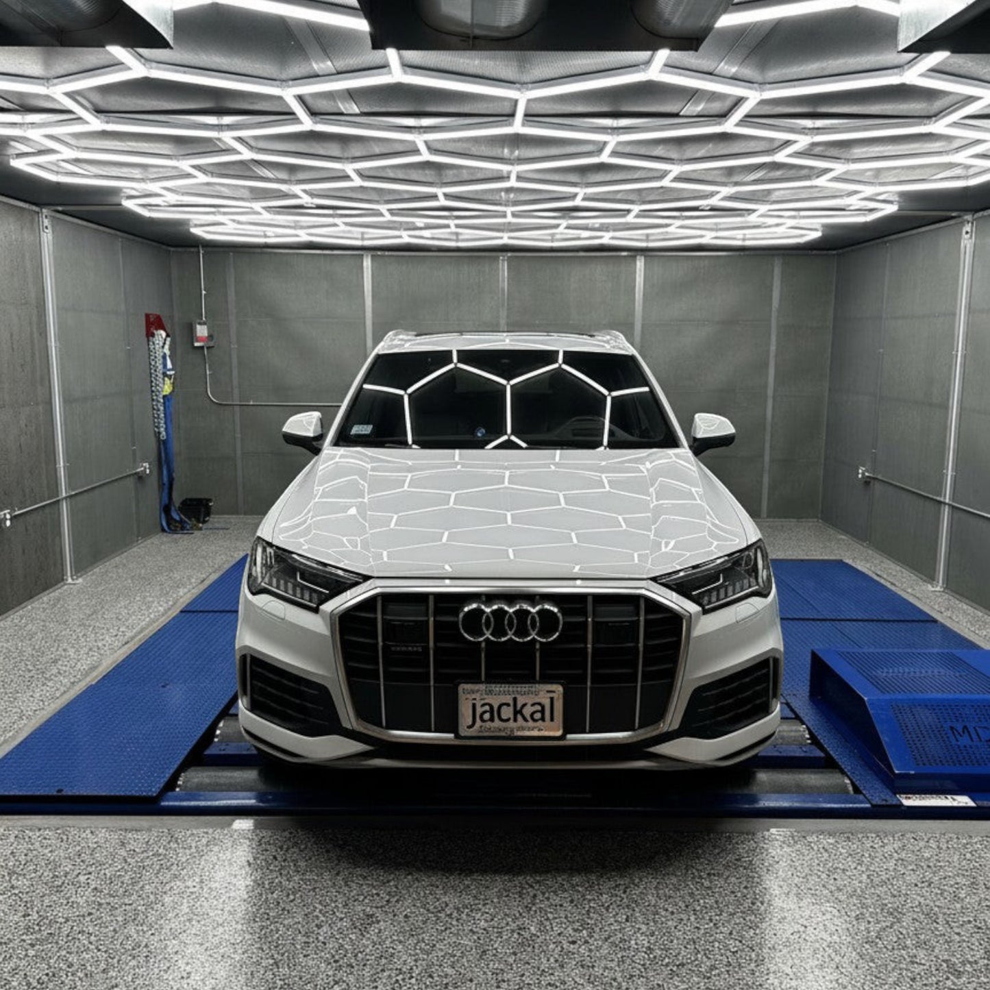 HS Tuning white Audi Q7 SUV positioned on a dynamometer in a professional garage with hexagonal ceiling lighting.