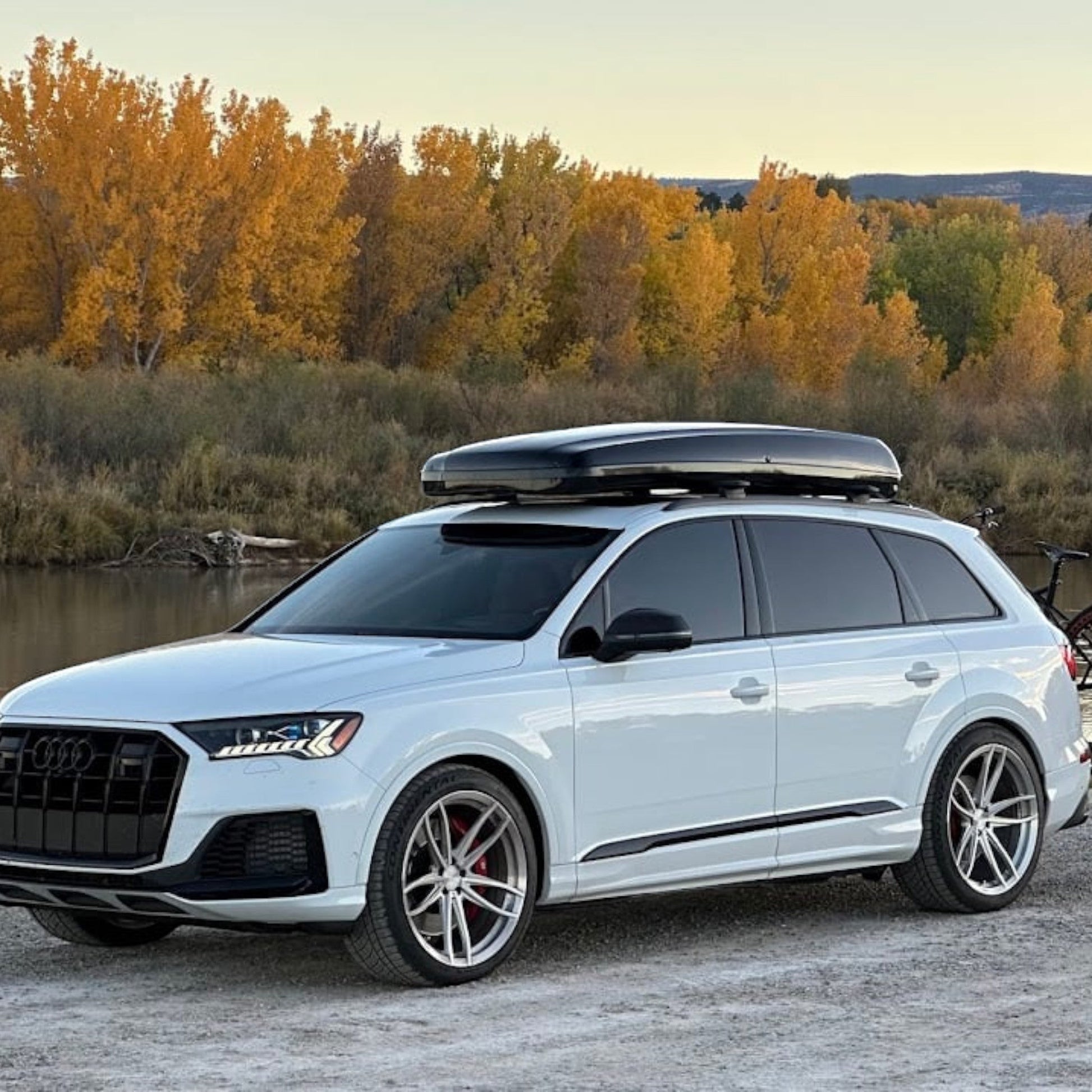 HS Tuning performance tune for white Audi SQ7 SUV with roof box and bike rack parked by a river in autumn.