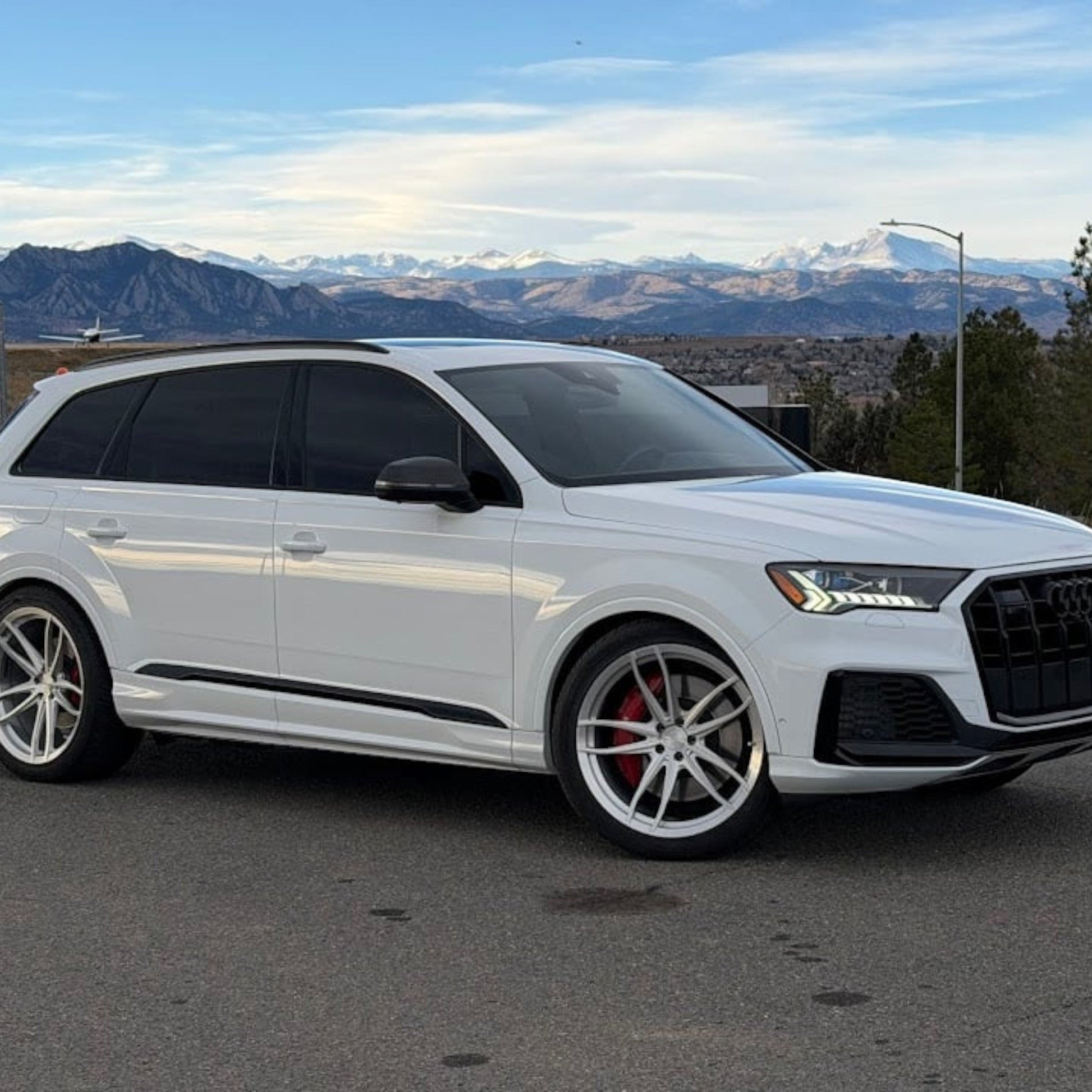 HS Tuning performance white Audi SQ7 SUV with custom wheels parked against a scenic mountain backdrop.